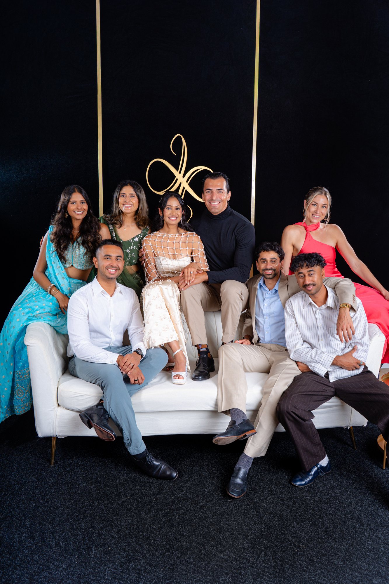 Eight guests in formal and traditional attire posed on and around the white sofa of the Portrait Lounge