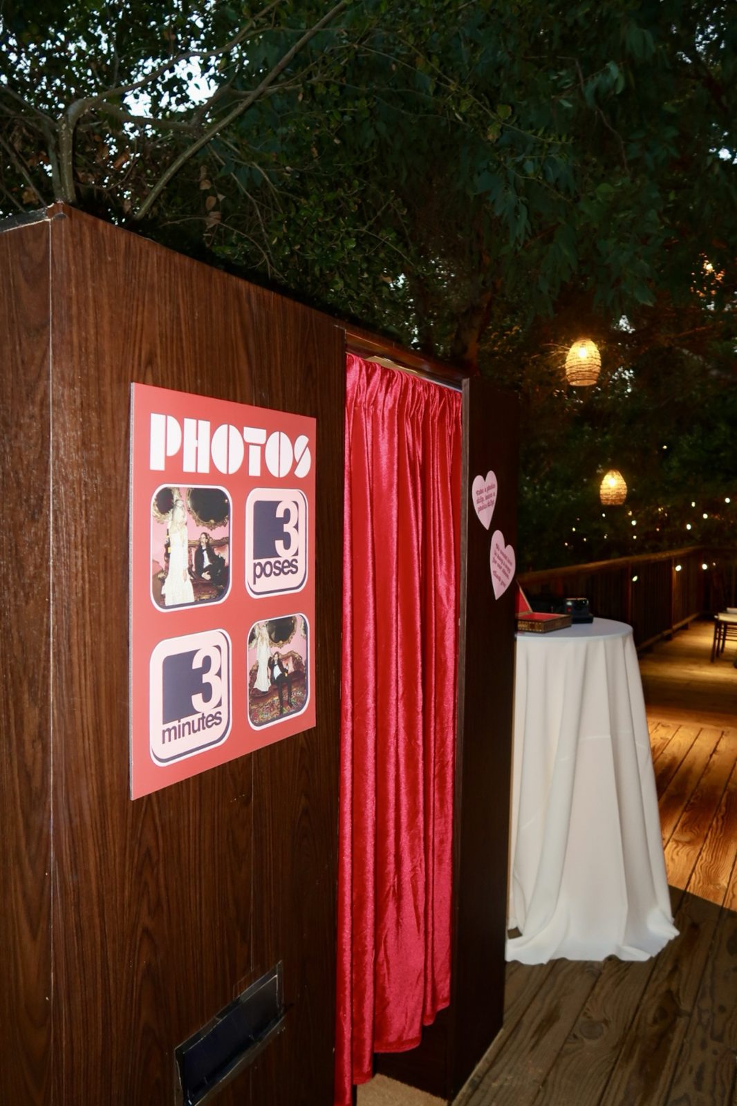 Wood-grain Vintage Booth with a red velvet curtain and a retro Photos poster on a deck under oak trees at Calamigos Ranch